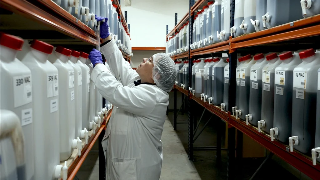 Technicienne en blouse blanche manipulant des bidons dans un laboratoire de production industrielle, extrait vidéo de lagence de communication vidéo Scriptonic