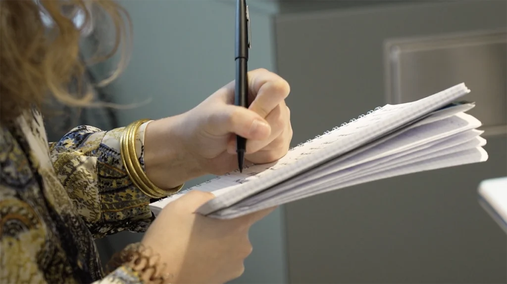prise-de-notes-collaborateur-scriptonic Main d’une collaboratrice prenant des notes pendant un tournage, image captée par Scriptonic